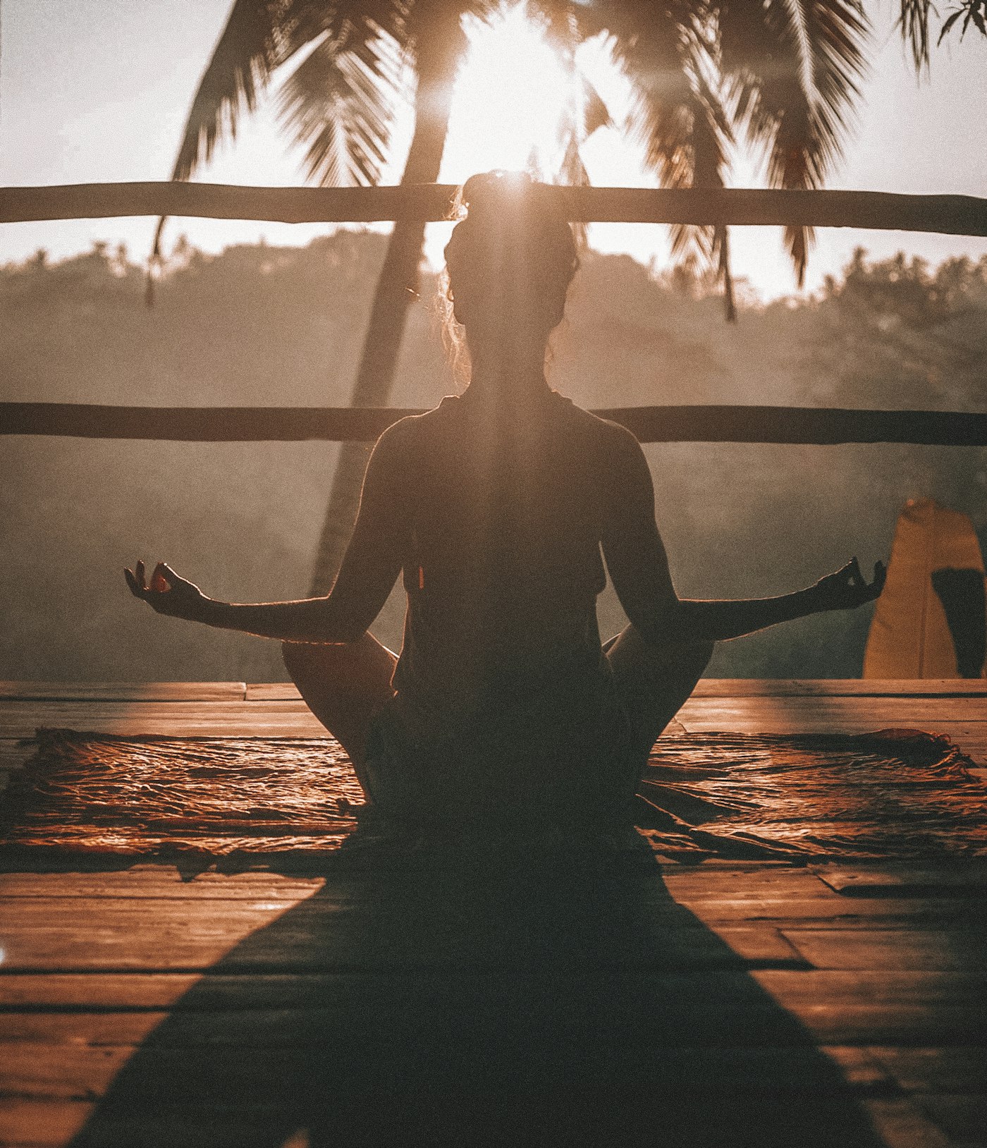 Silhouette of a person meditating in lotus pose at sunrise under palm trees