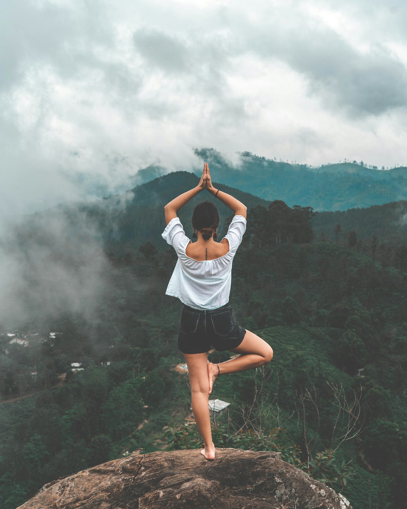Woman in tree pose on a rock overlooking misty green mountains