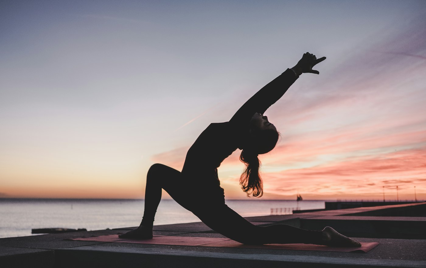 Silhouette of a person in a standing side bend at sunset by the water