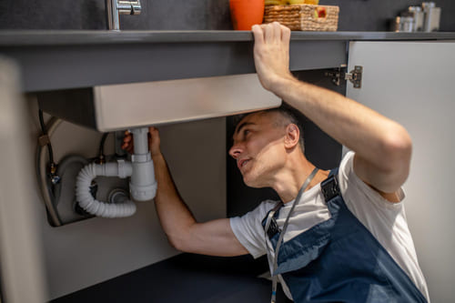 Plumber repairing pipework under a sink