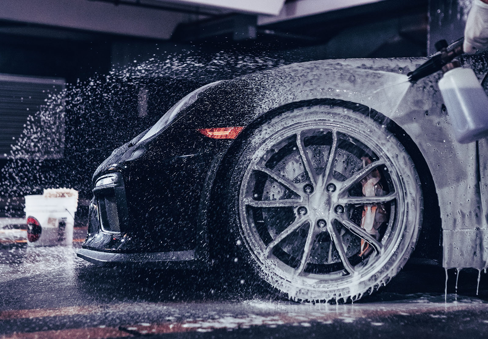 Snow foam cannon covering a black car before a hand wash