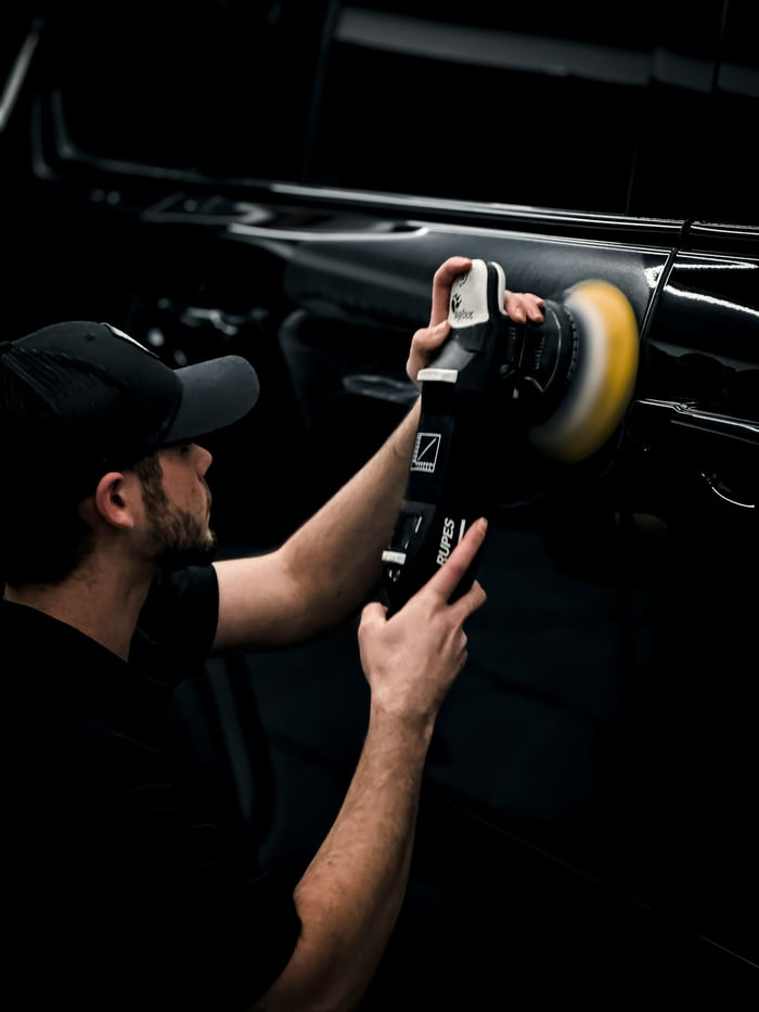 Detailer machine-polishing a black car panel