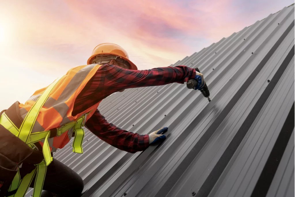 Roofer fastening standing-seam metal roofing at sunset