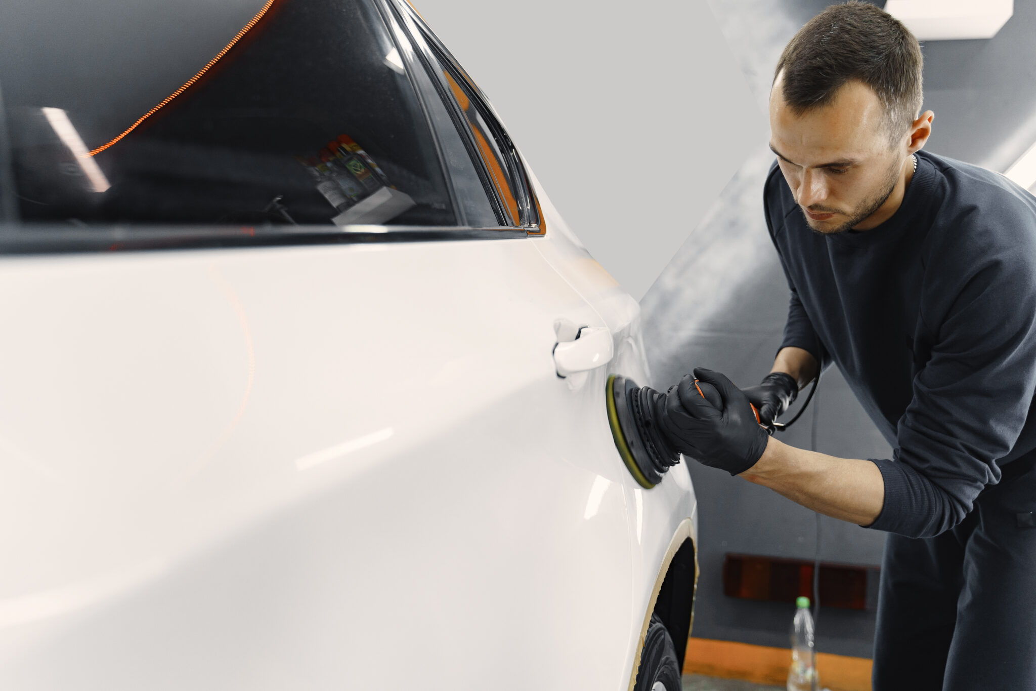 Detailer machine-polishing a white car in the studio