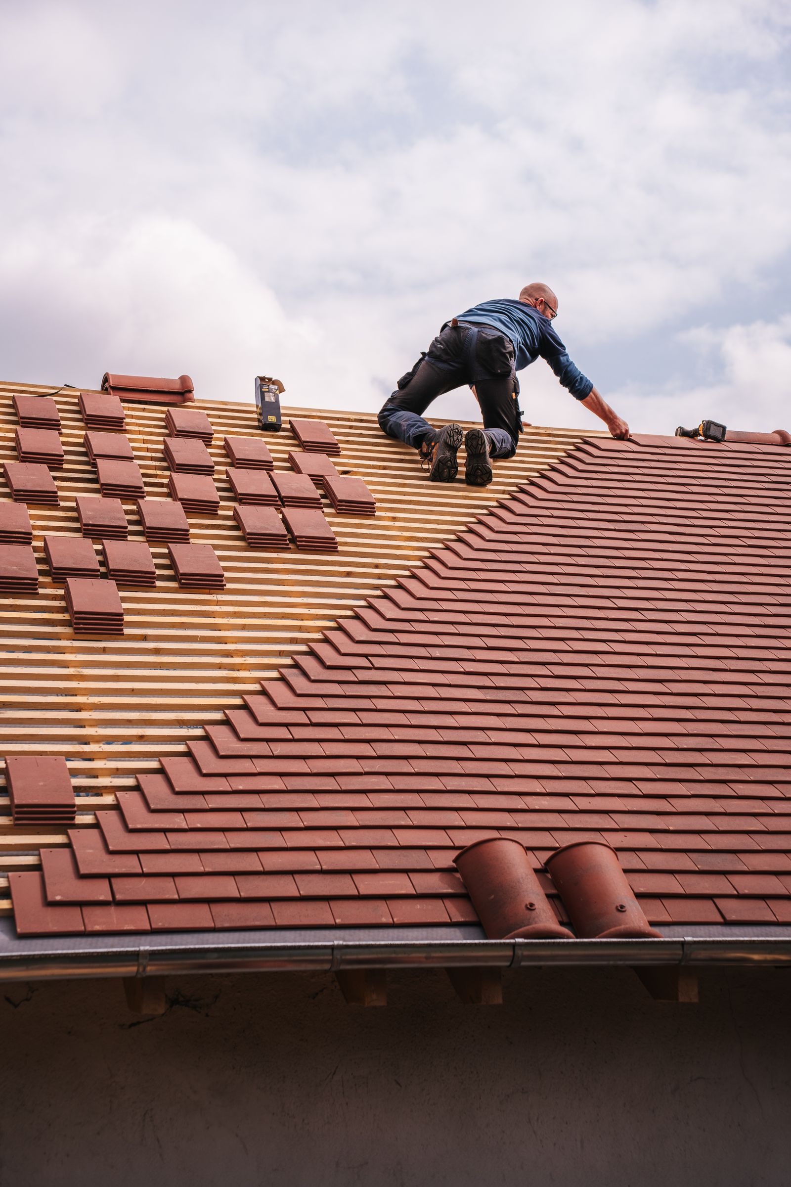 Roofer laying clay tiles on a pitched roof under a bright sky