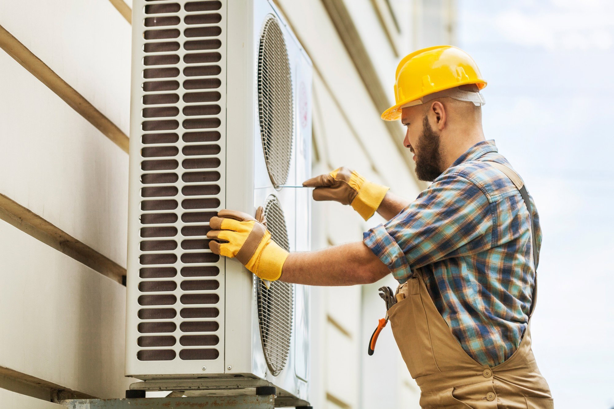 Technician in a hard hat servicing an outdoor air conditioning condenser unit