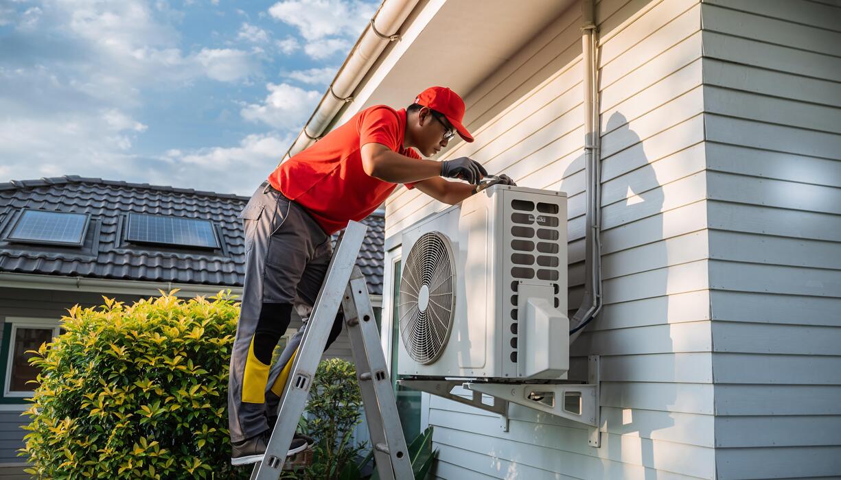 Technician installing an air conditioning unit on a house exterior