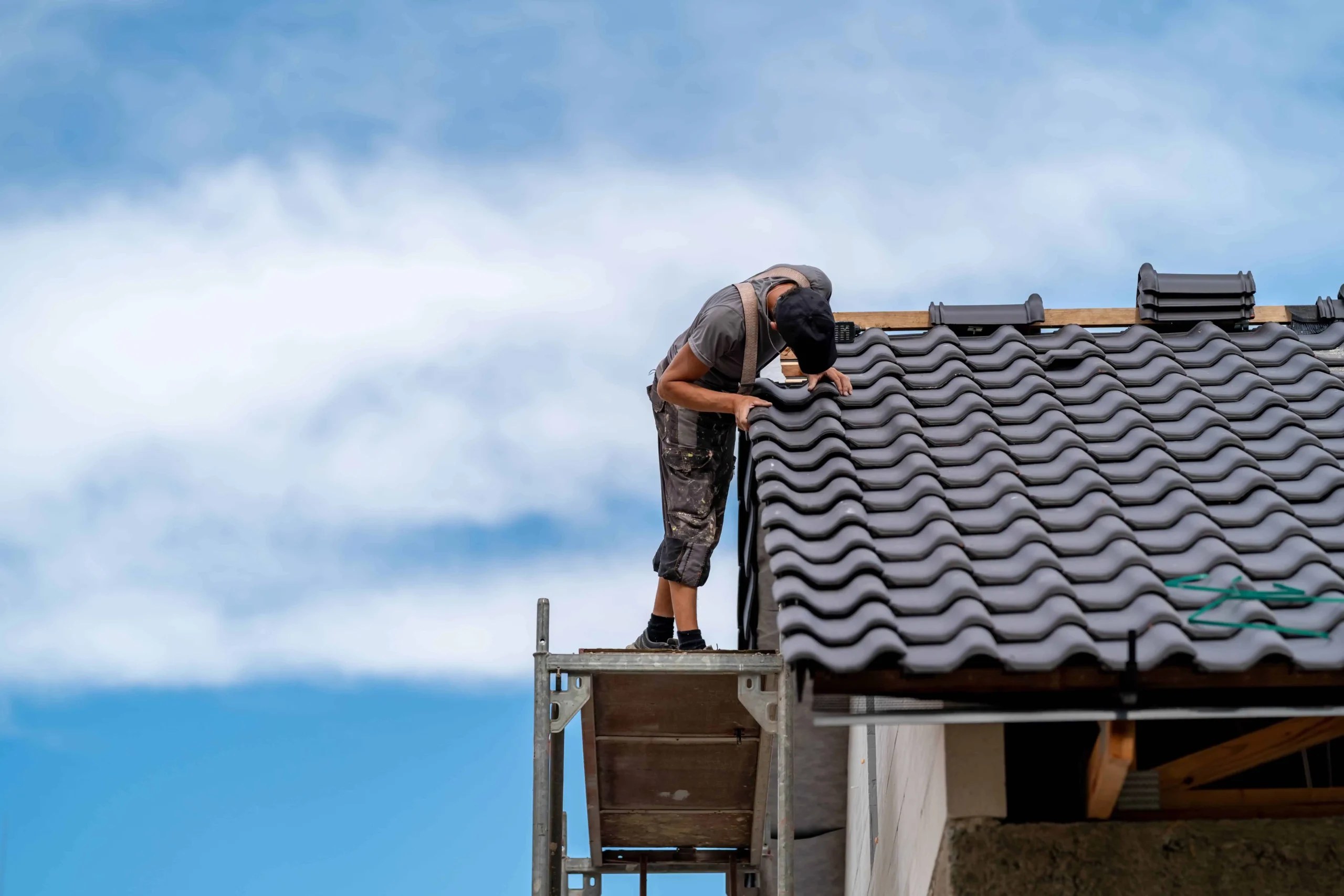 Roofer on scaffolding laying tiles on a pitched roof