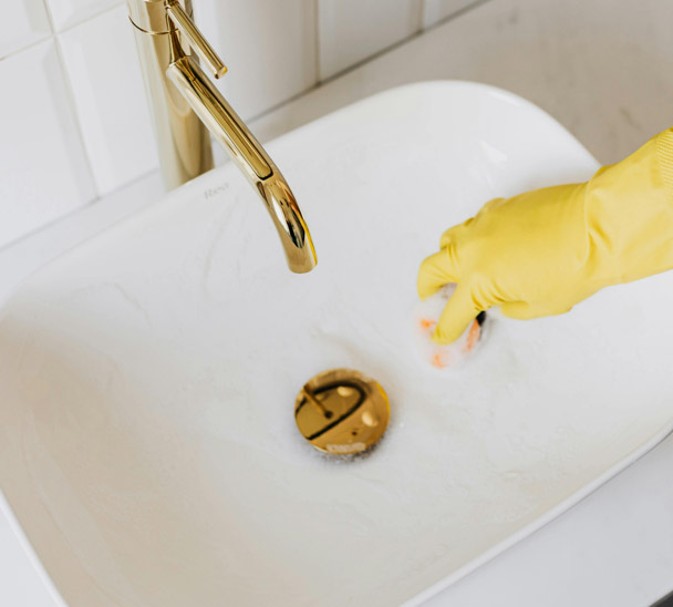 Gloved hand cleaning a sink drain