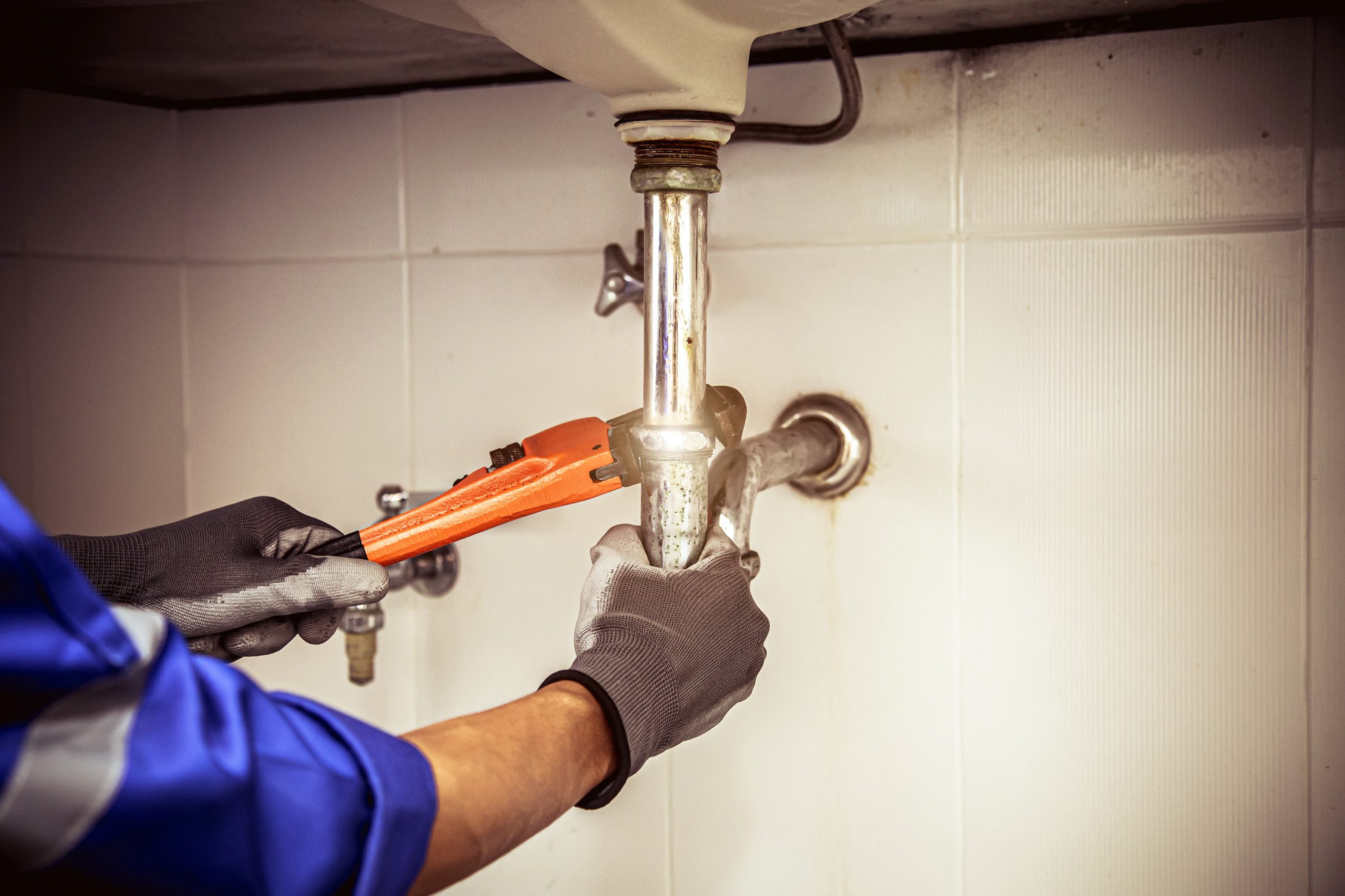Plumber tightening a pipe fitting under a sink