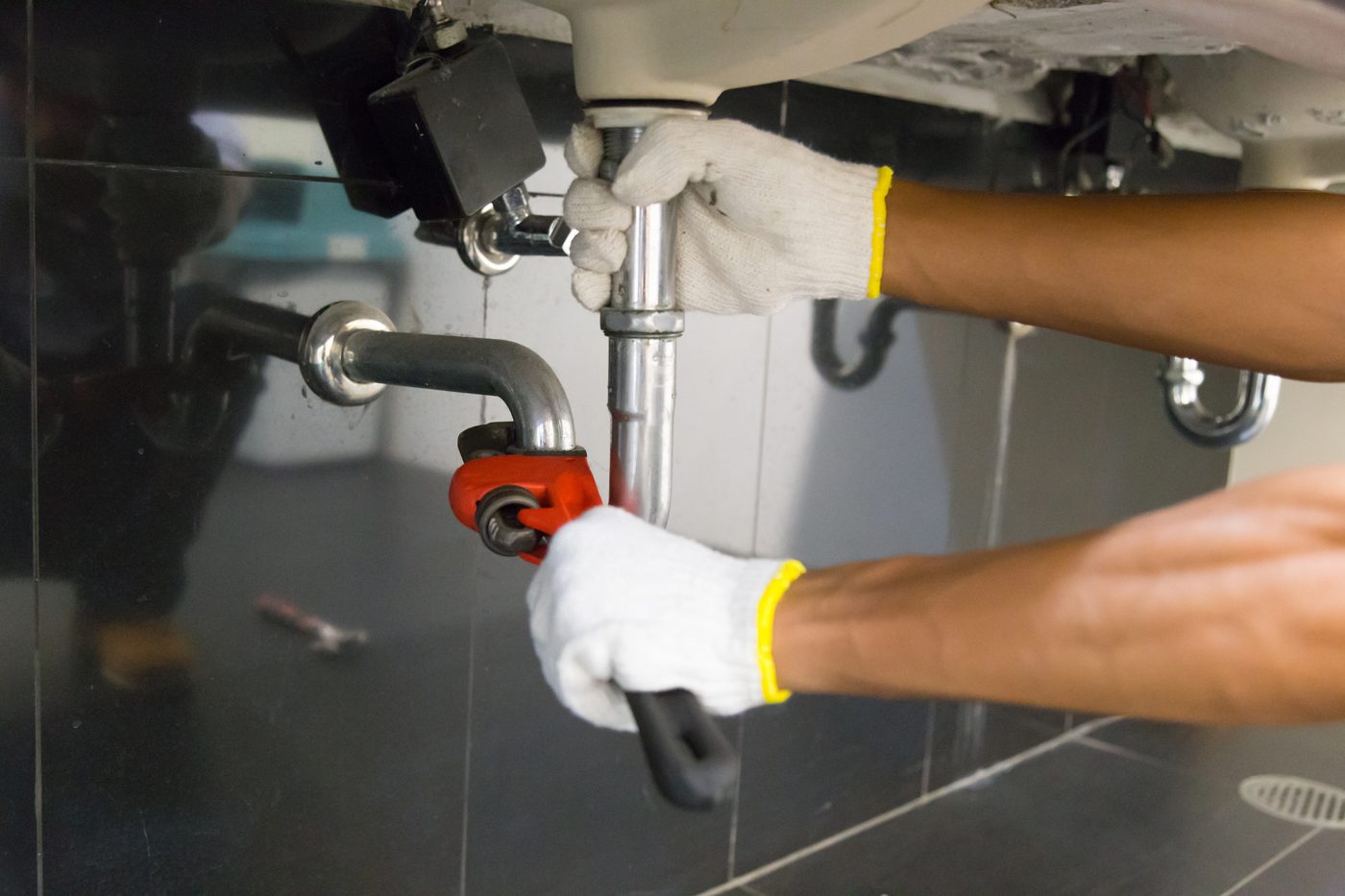 Plumber's hands fitting a sink trap with a pipe wrench