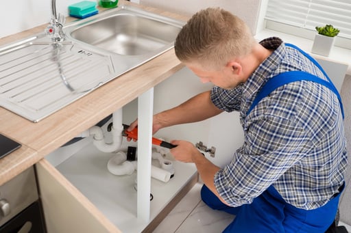 Plumber repairing pipework beneath a kitchen sink