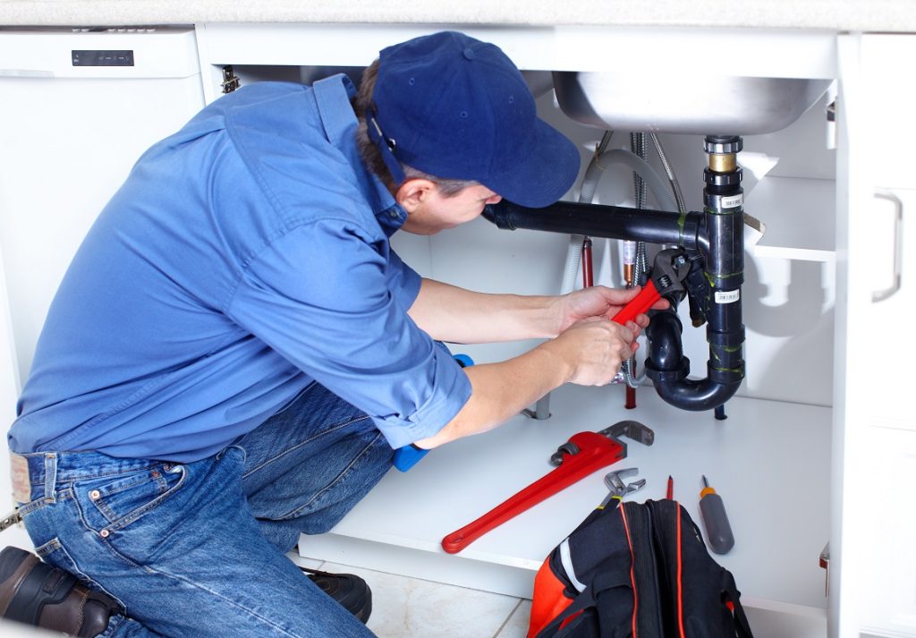 Plumber repairing pipework under a sink