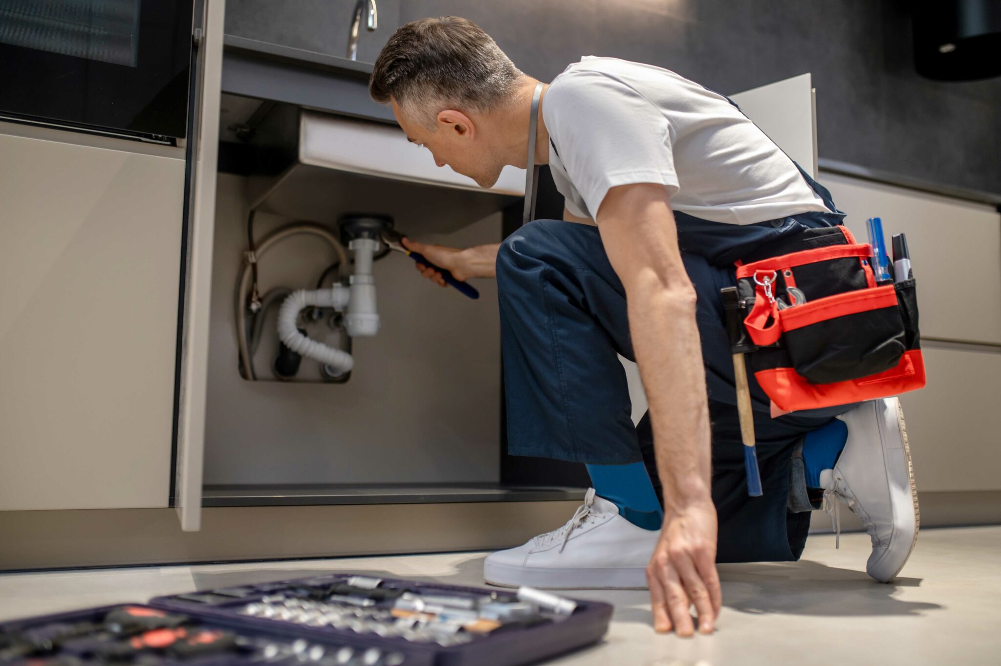 Plumber repairing a kitchen sink pipe with a wrench (illustrative concept imagery)