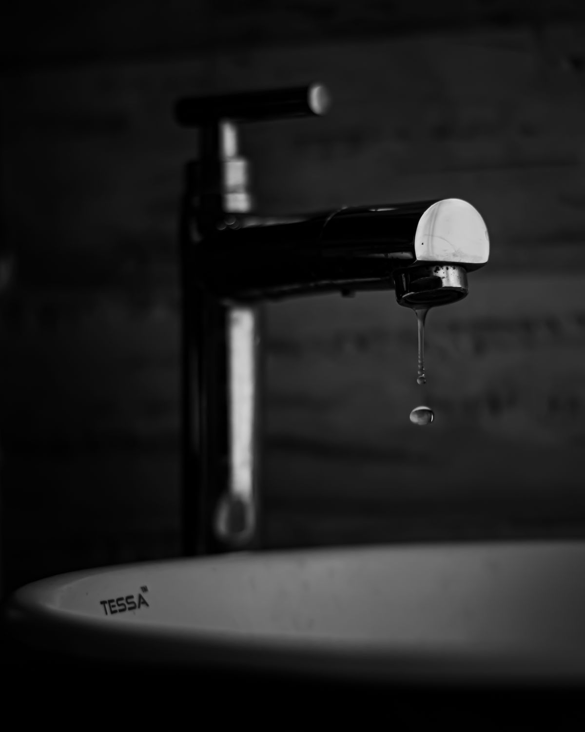 Water dripping from a bathroom faucet in black and white