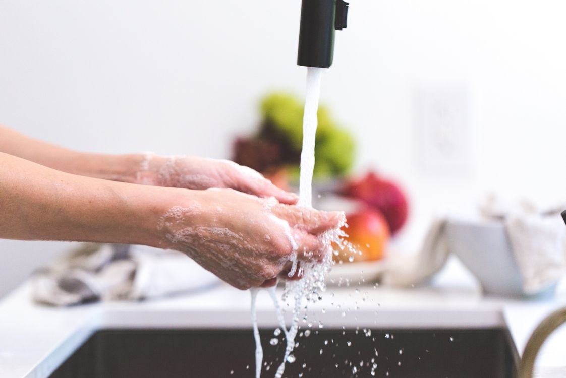 Hands rinsing under a running kitchen faucet