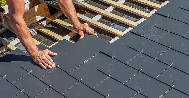 Hands laying dark slates on roof battens