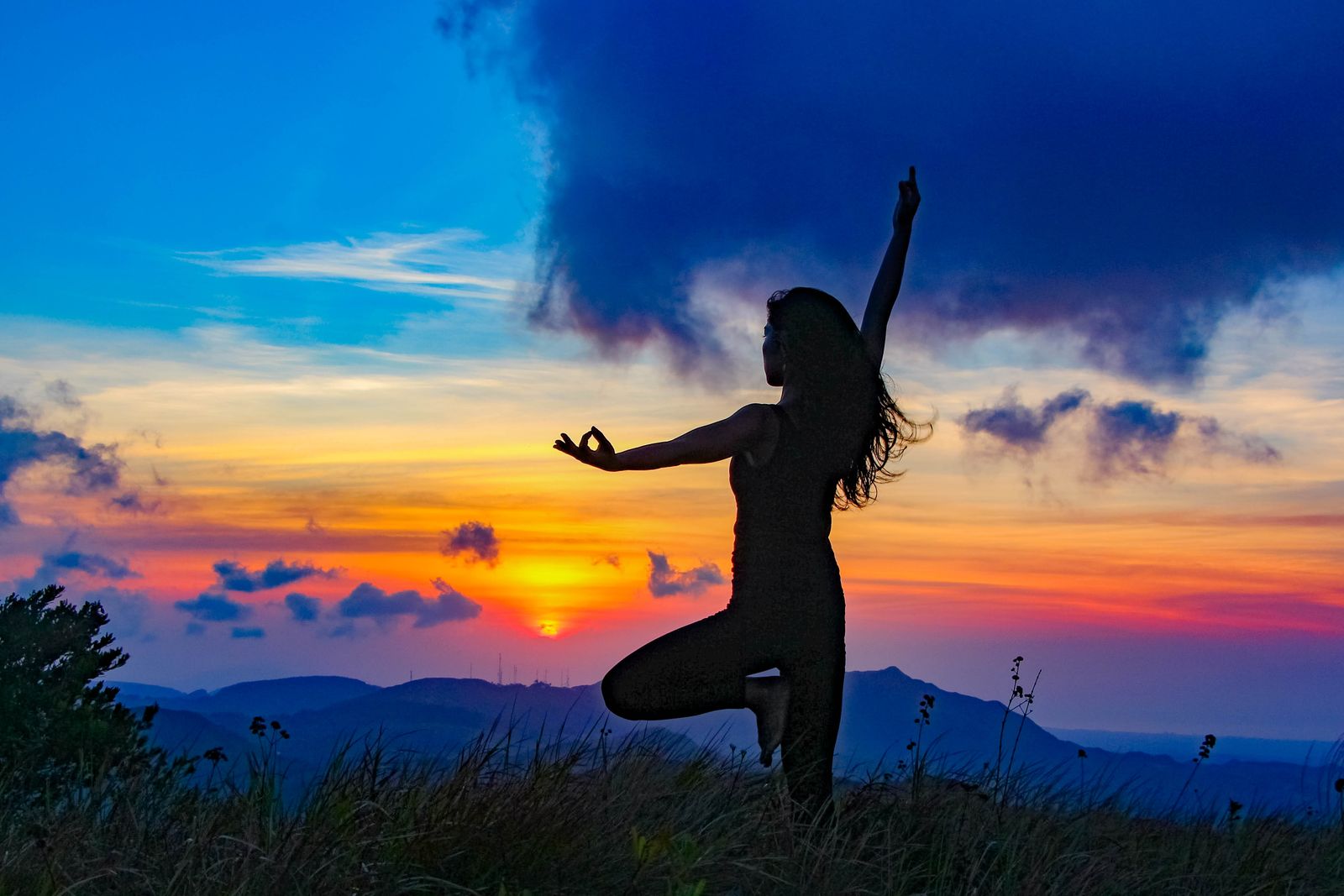 A person practicing tree pose in yoga silhouette against a desert sunset