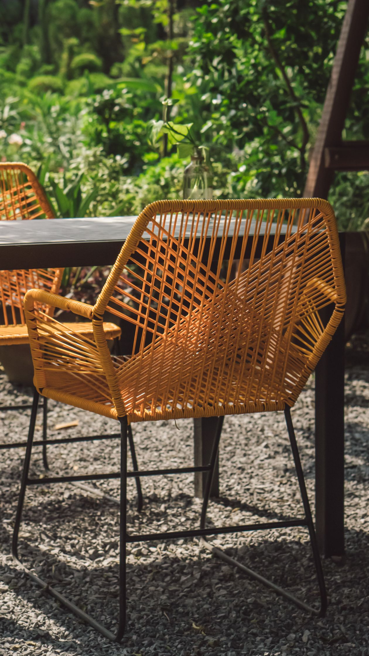Rattan chairs on a gravel patio surrounded by lush garden planting