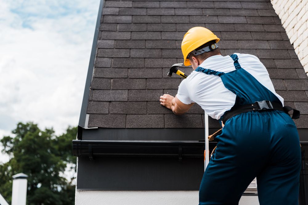 Roofer nailing shingles along the ridge of a house