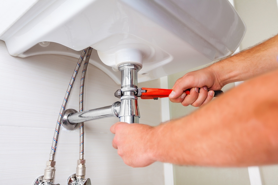 Plumber's hands tightening a pipe fitting under a sink
